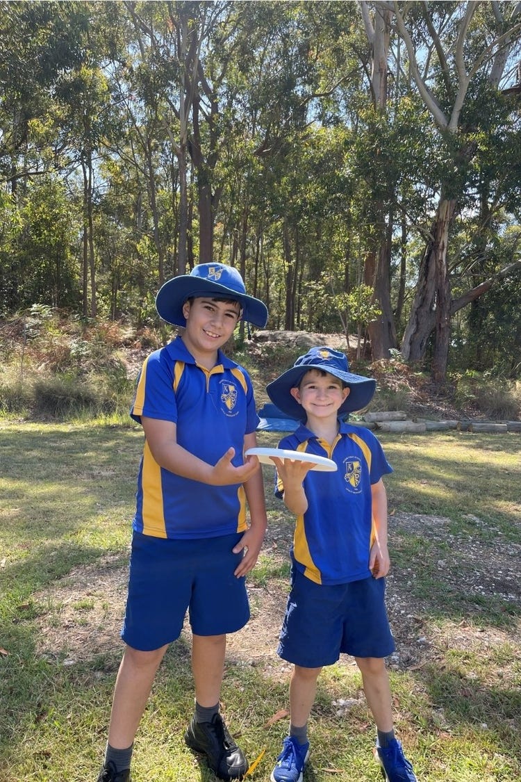 Hillside students holding a Frisby on the bottom oval in front of the bush